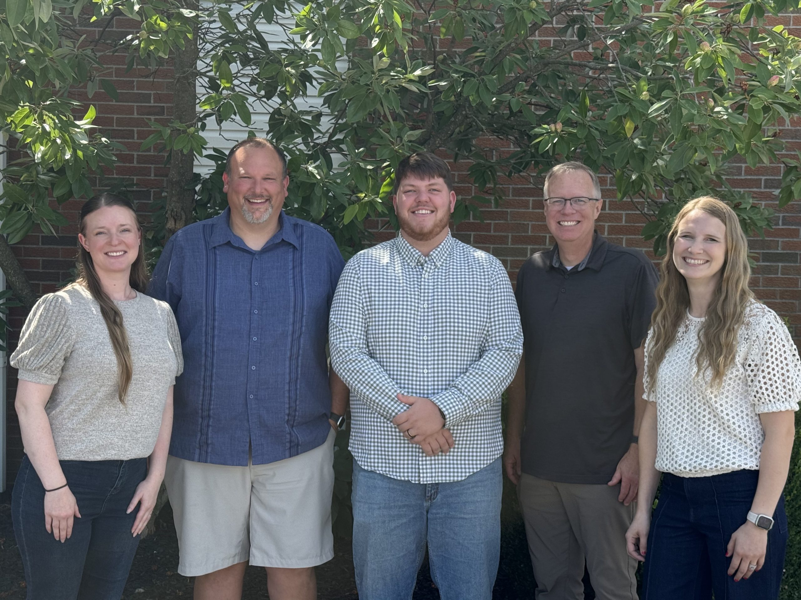 An outdoor photo featuring four staff members: two men on either end, two women in the middle.